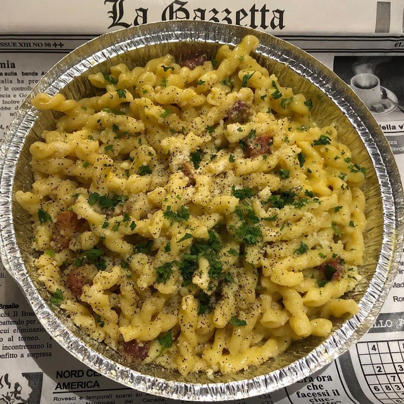 Becca's Kitchen's cavatappi pasta with creamy cheese sauce, sausage, pepper, and parsley in a foil container.