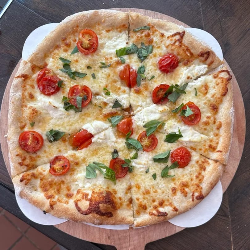 Becca's Kitchen's white pizza with cherry tomatoes and fresh basil, served on a wooden board.