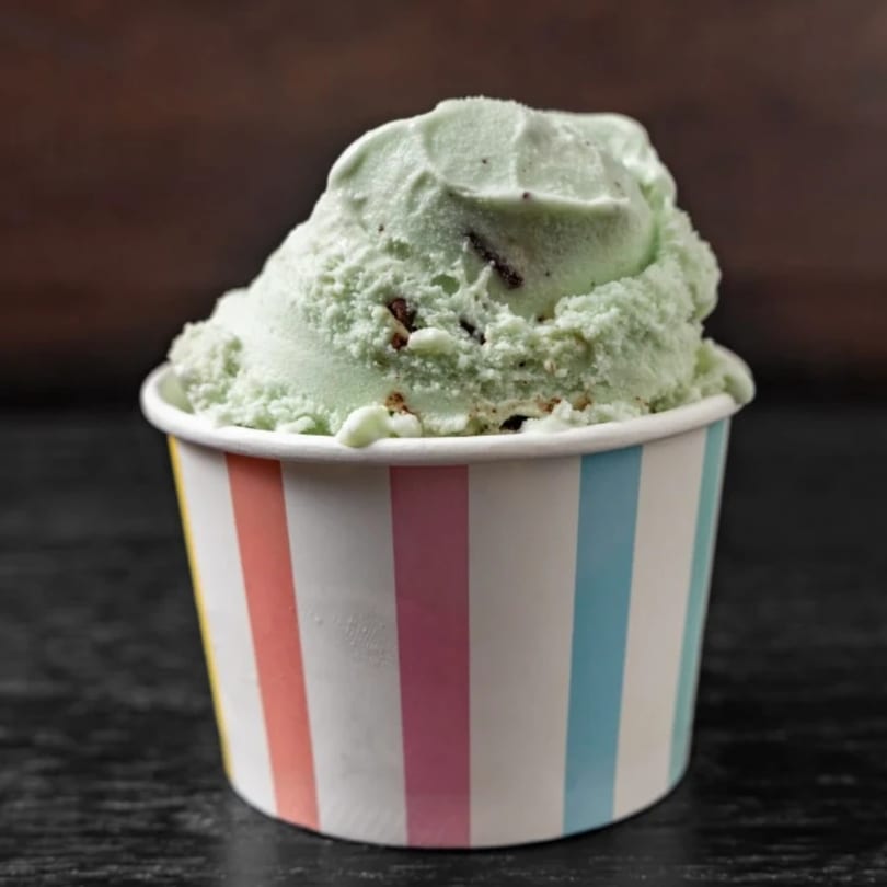Mint chocolate chip gelato in a colorful striped cup on a dark surface.